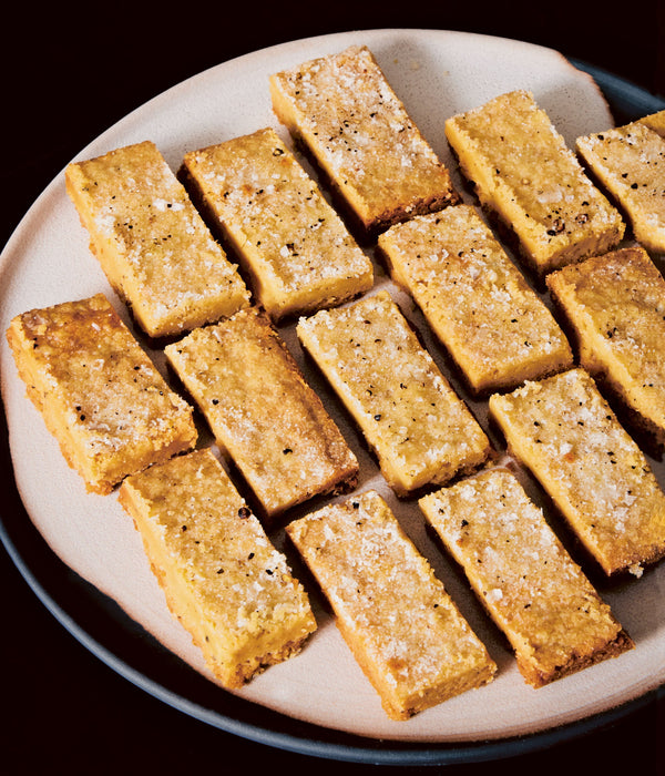 Plate of around a dozen light orange colored rectangular shortbread pastries. 
