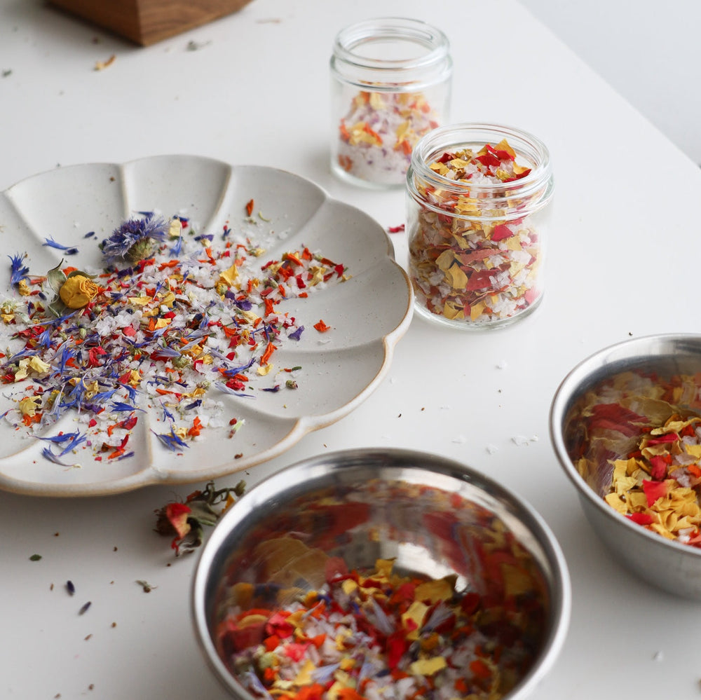 Violet, yellow and red flower petals and flake salt, in jars, bowls and decorative plate.
