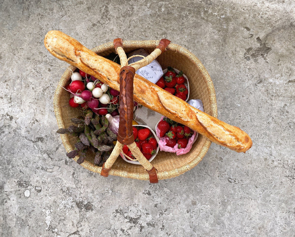 A wicker basket filled with fresh produce and a baguette.