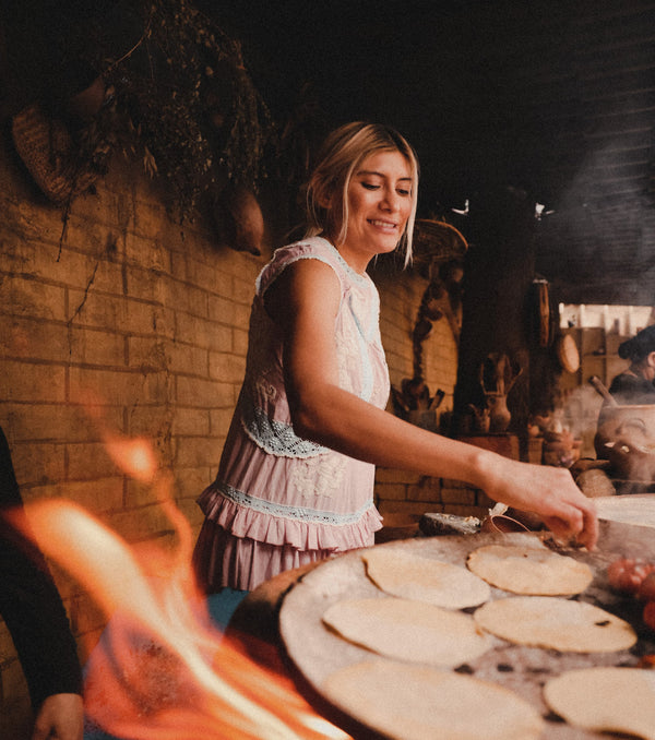 A woman stands and smiles while cooking.