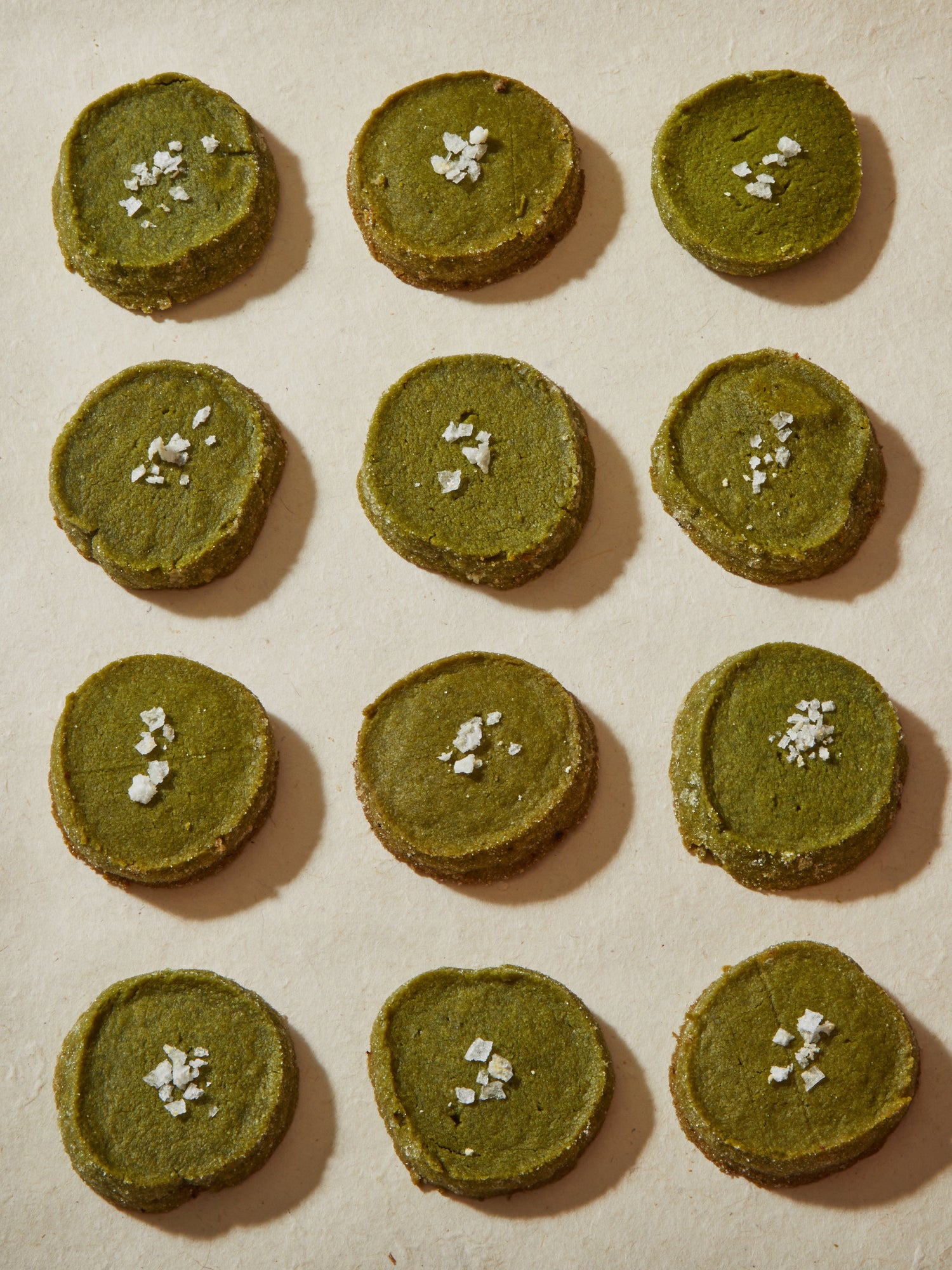 A dozen round green cookies, each topped with flake salt.