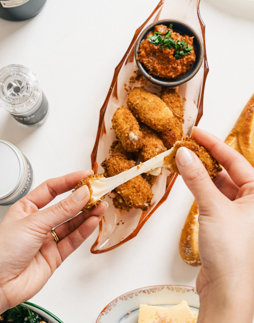 Mozzarella sticks plated with marinara sauce. Two hands are pulling apart a mozzarella stick and showcasing the stretchy cheese within.