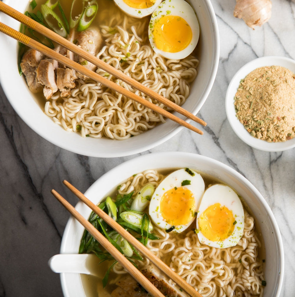 Two bowls of ramen topped with chicken, boiled eggs, and green onions.