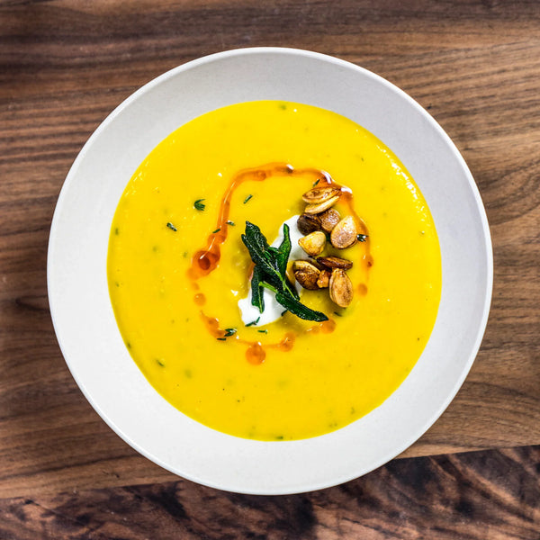 Bowl of yellow soup, topped with garnish and seeds in a white bowl