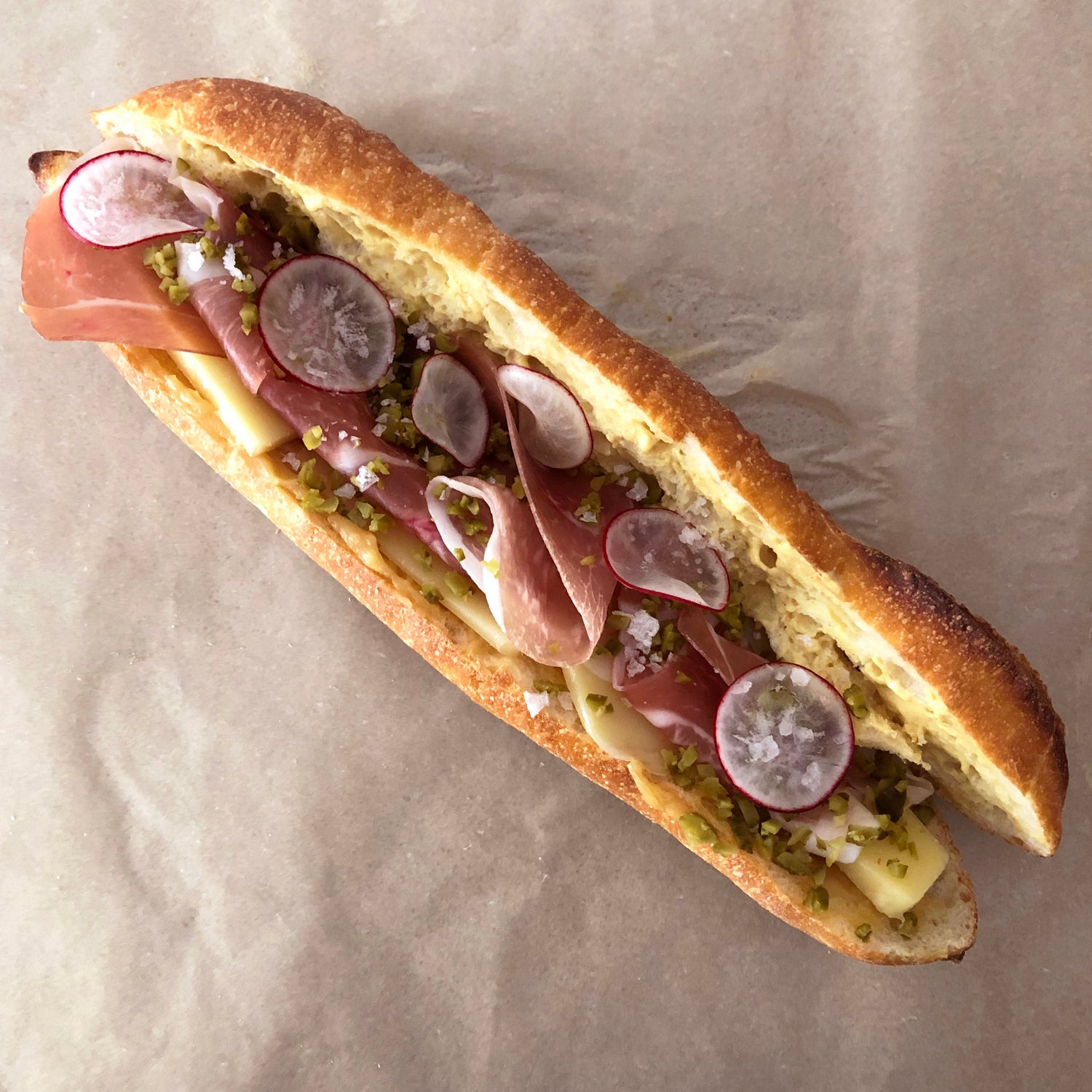 A ham and cheese sandwich with radishes and honey butter on a baguette.