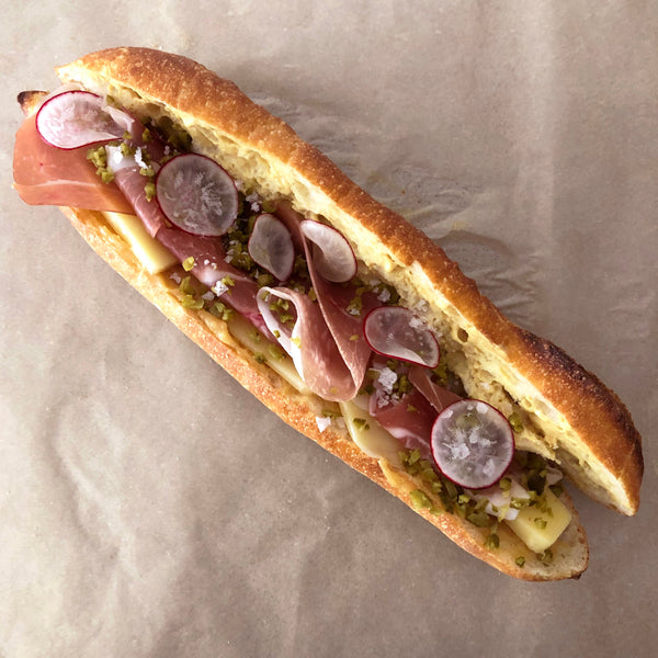 A ham and cheese sandwich with radishes and honey butter on a baguette.