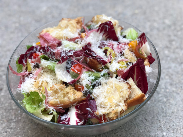A bowl of Italian panzanella salad with greens, crusty bread, and parmesan.