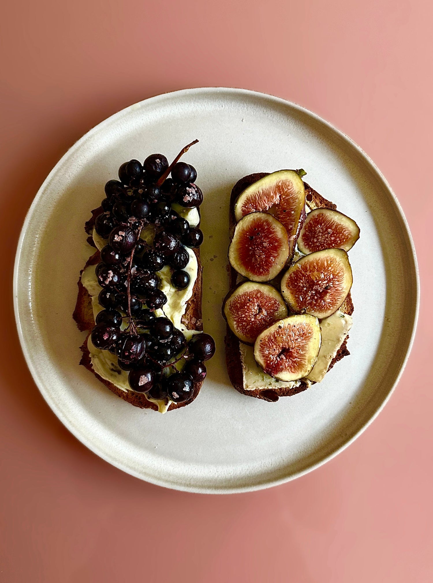 A plate with two pieces of toast, one with grapes and one with figs.