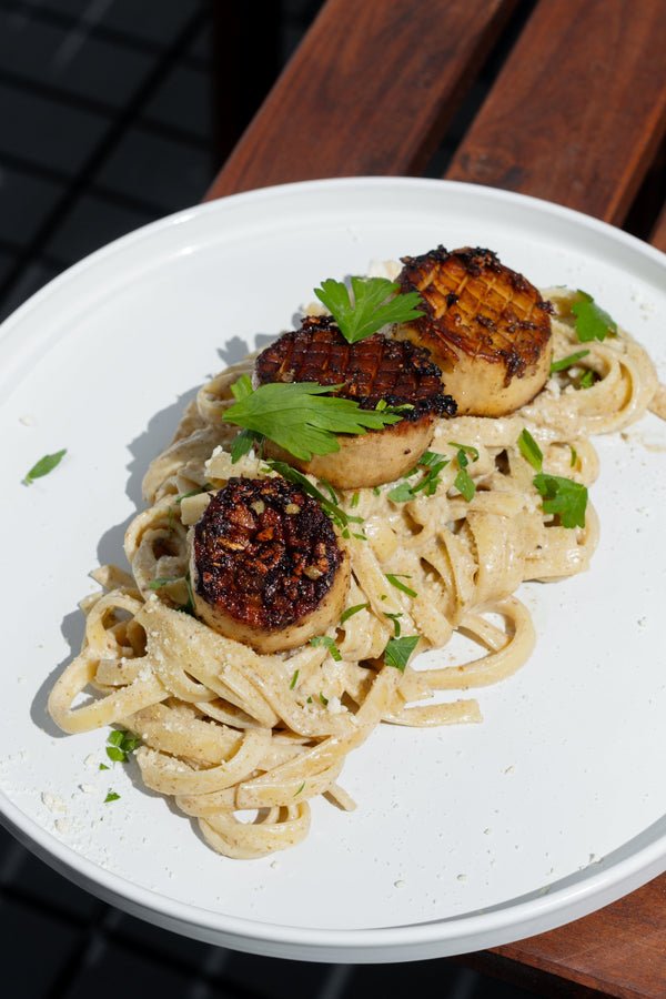 A white plate with Alfredo pasta, oyster mushroom stems, and parsley.