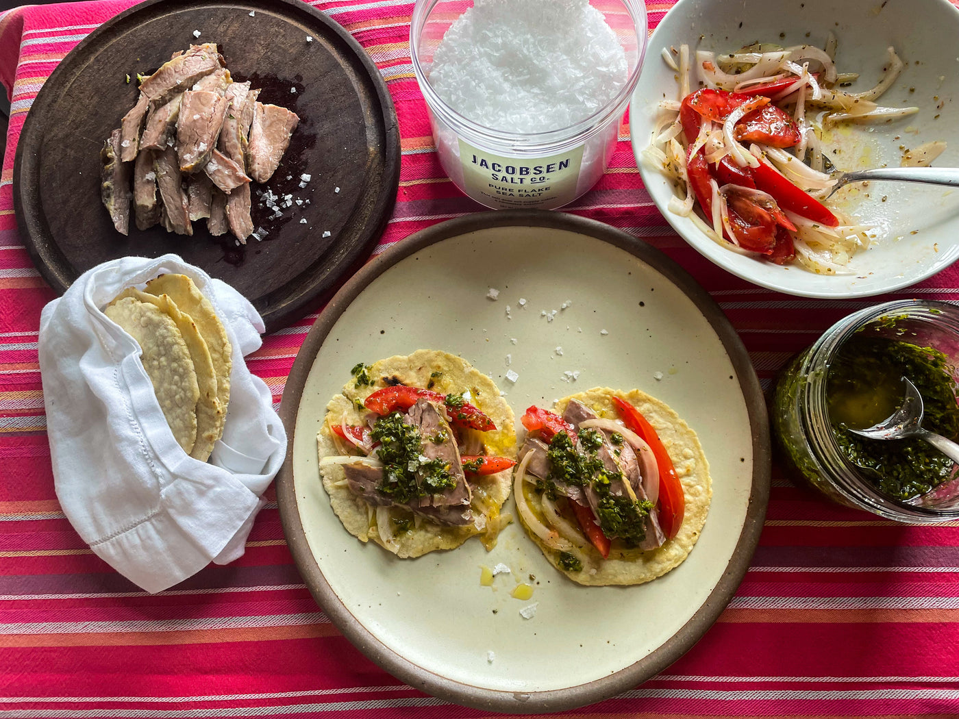 Plates of ingredients, including salt, surrounding a plate of constructed tacos.