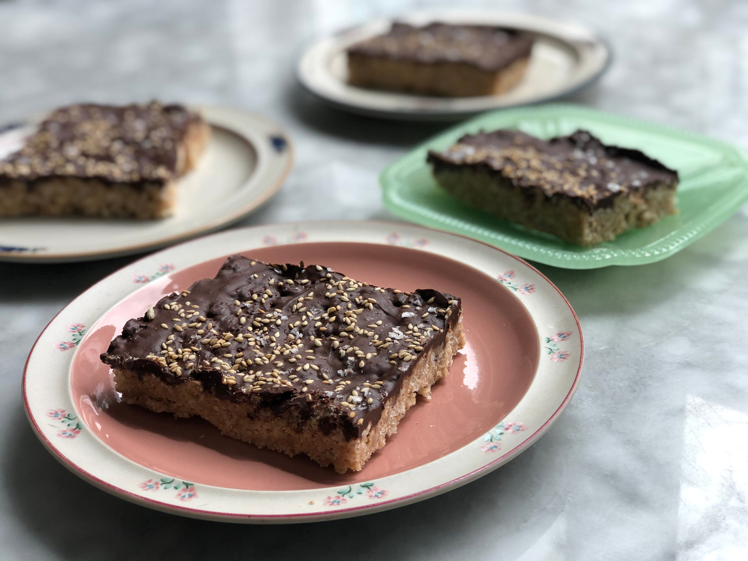 Four plates with slices of salty tahini rice crispy bars.