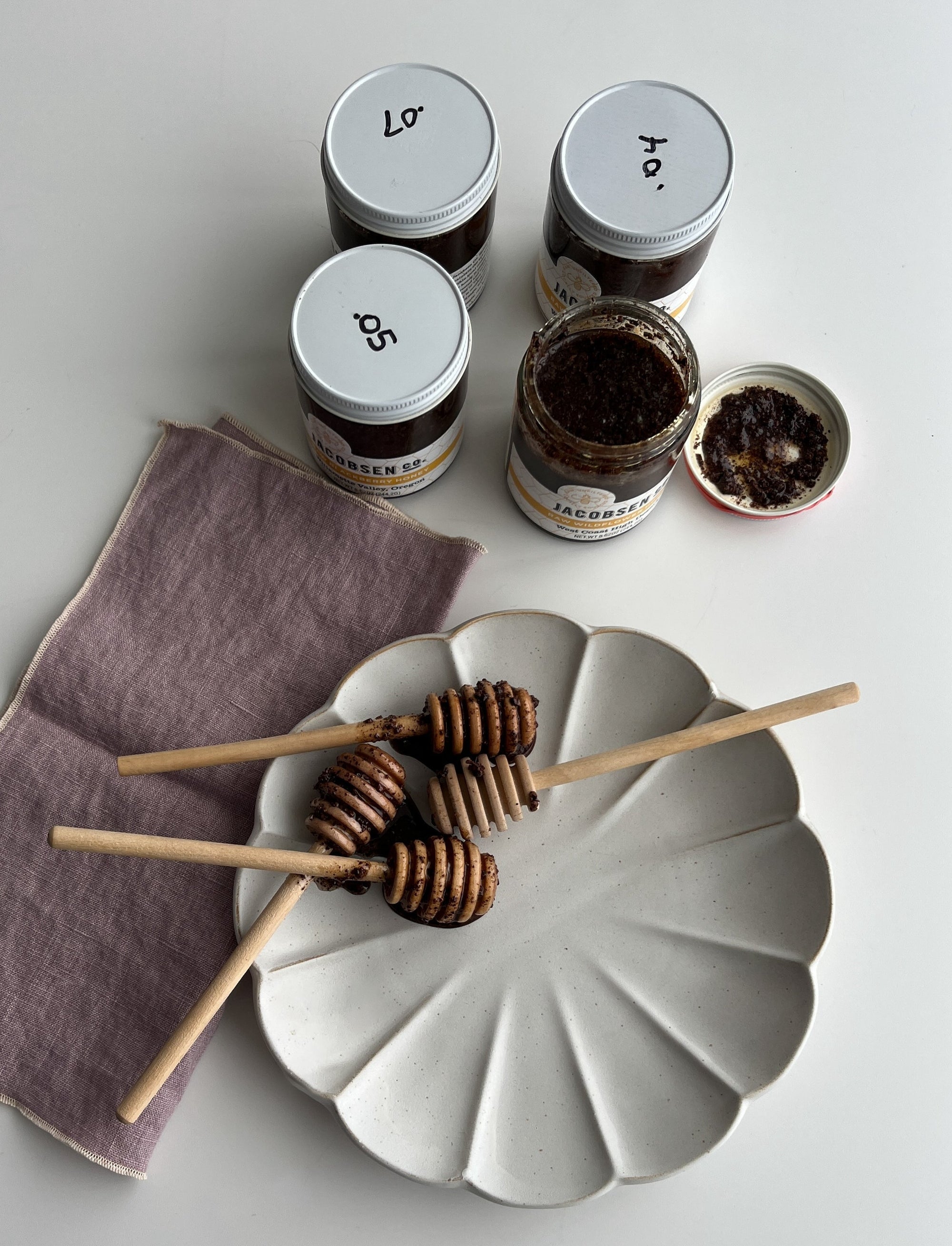 Jars of honey, with honey dippers on a decorative plate below.