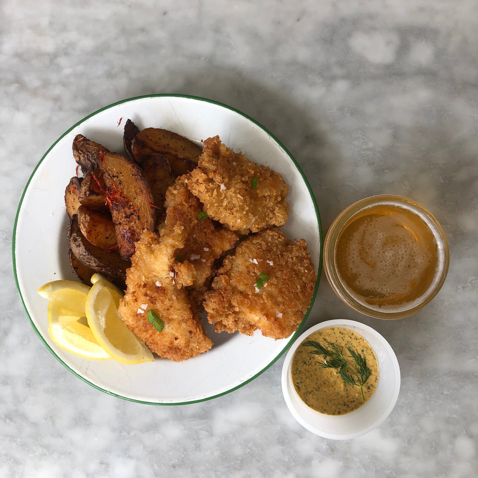 Potato wedges, lemon slices, and fried dish on a round white plate.