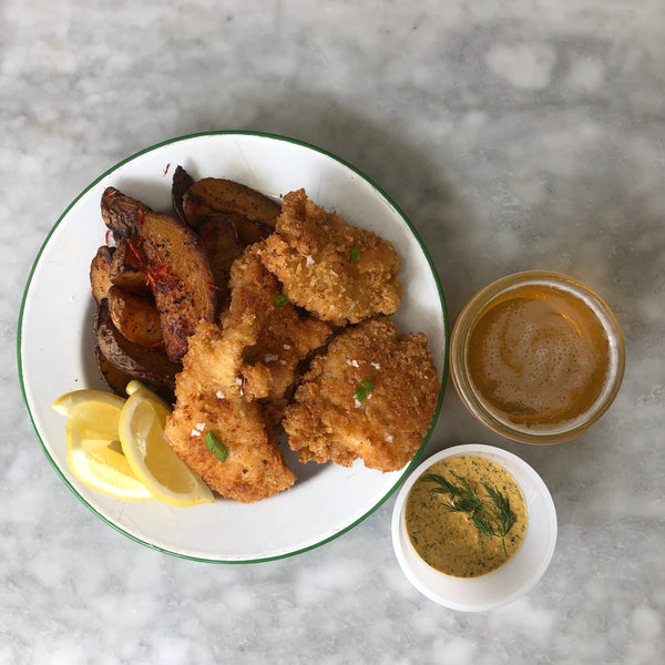 Potato wedges, lemon slices, and fried dish on a round white plate.