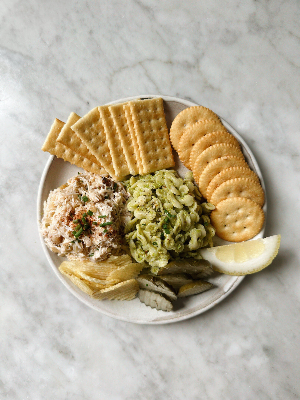 Plate with circular and rectangular crackers, next to various dips and toppings.