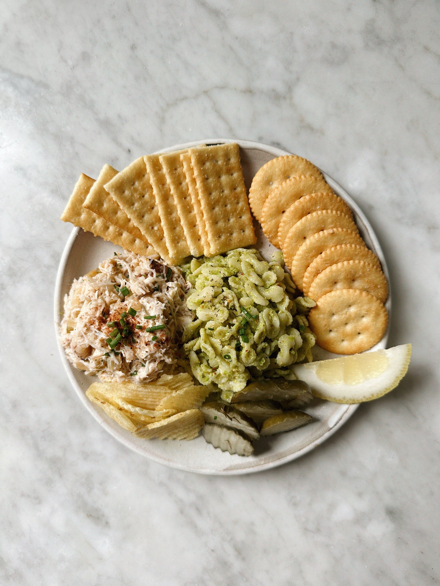 Plate with circular and rectangular crackers, next to various dips and toppings.