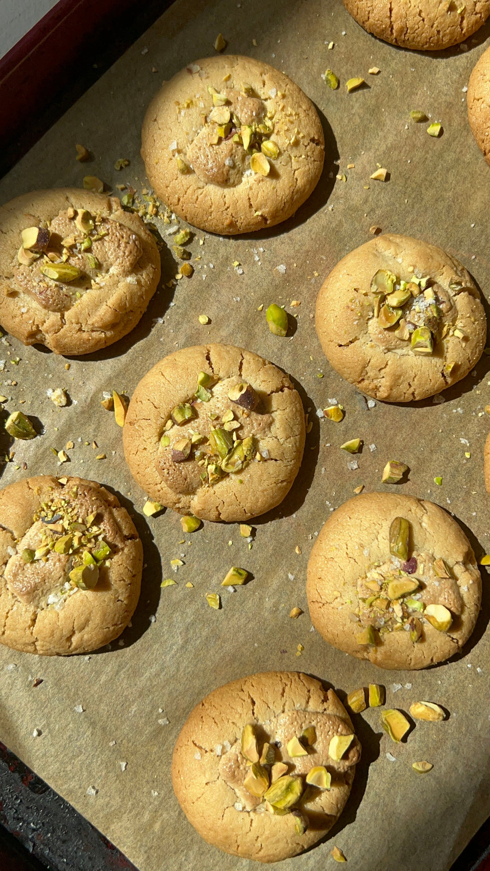 Several light green cookies, topped with crumbled pistachios.