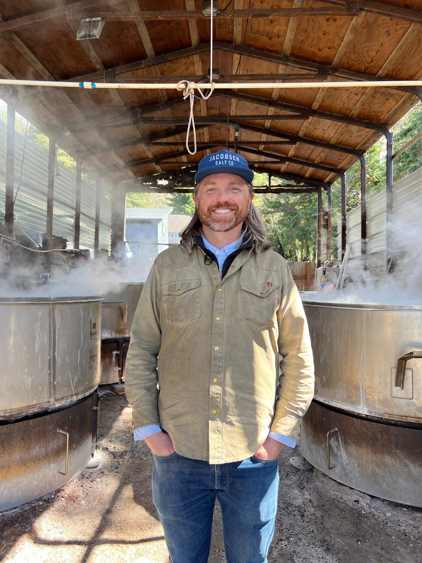 A man stands in a shed next to large containers for making salt.