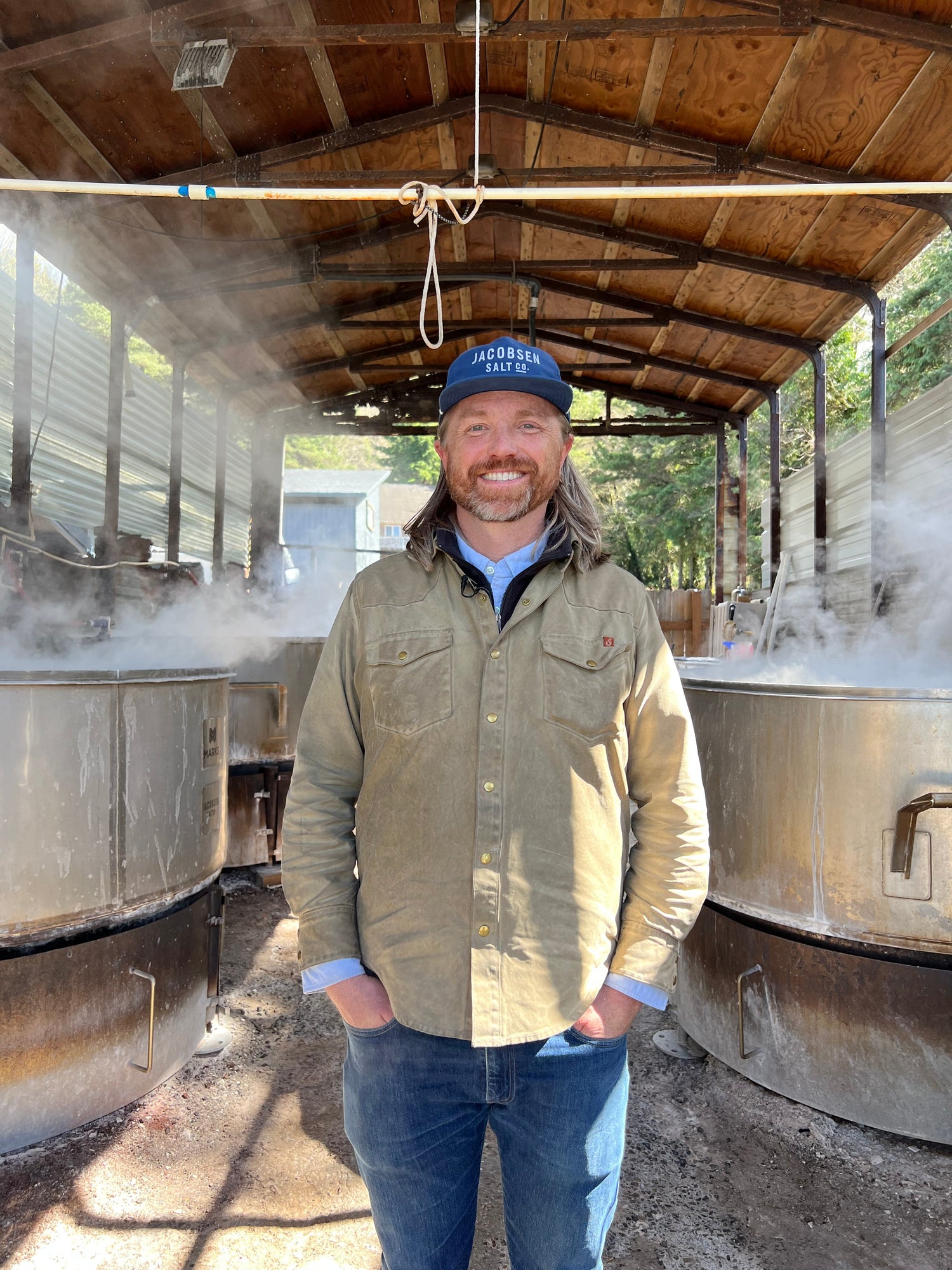 A man stands in a shed next to large containers for making salt.
