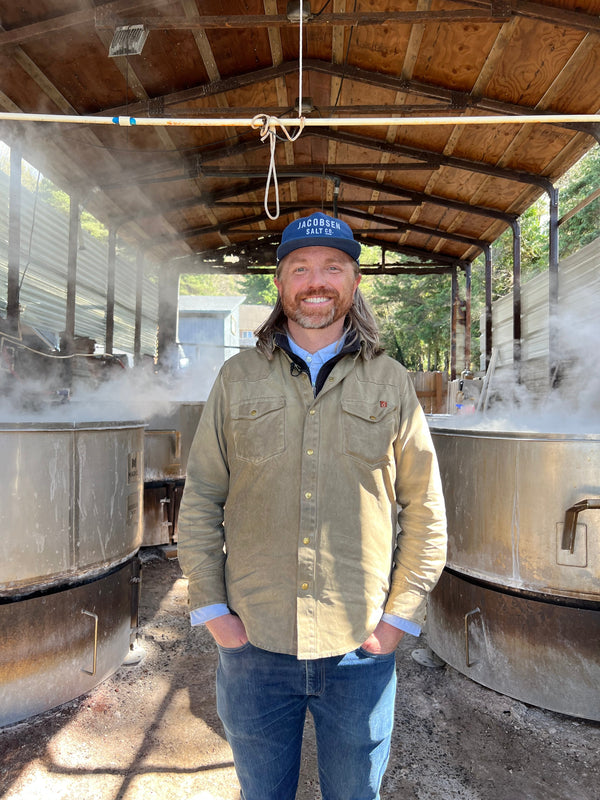 A man stands in a shed next to large containers for making salt.