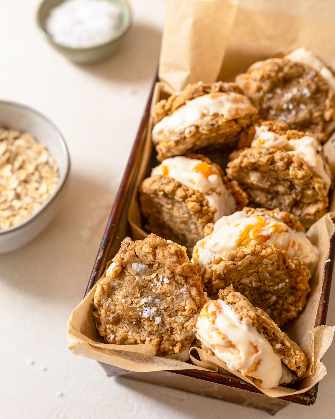 Several oatmeal ice cream sandwiches in a glass serving dish. Visible flakes of salt top the oatmeal cookies.