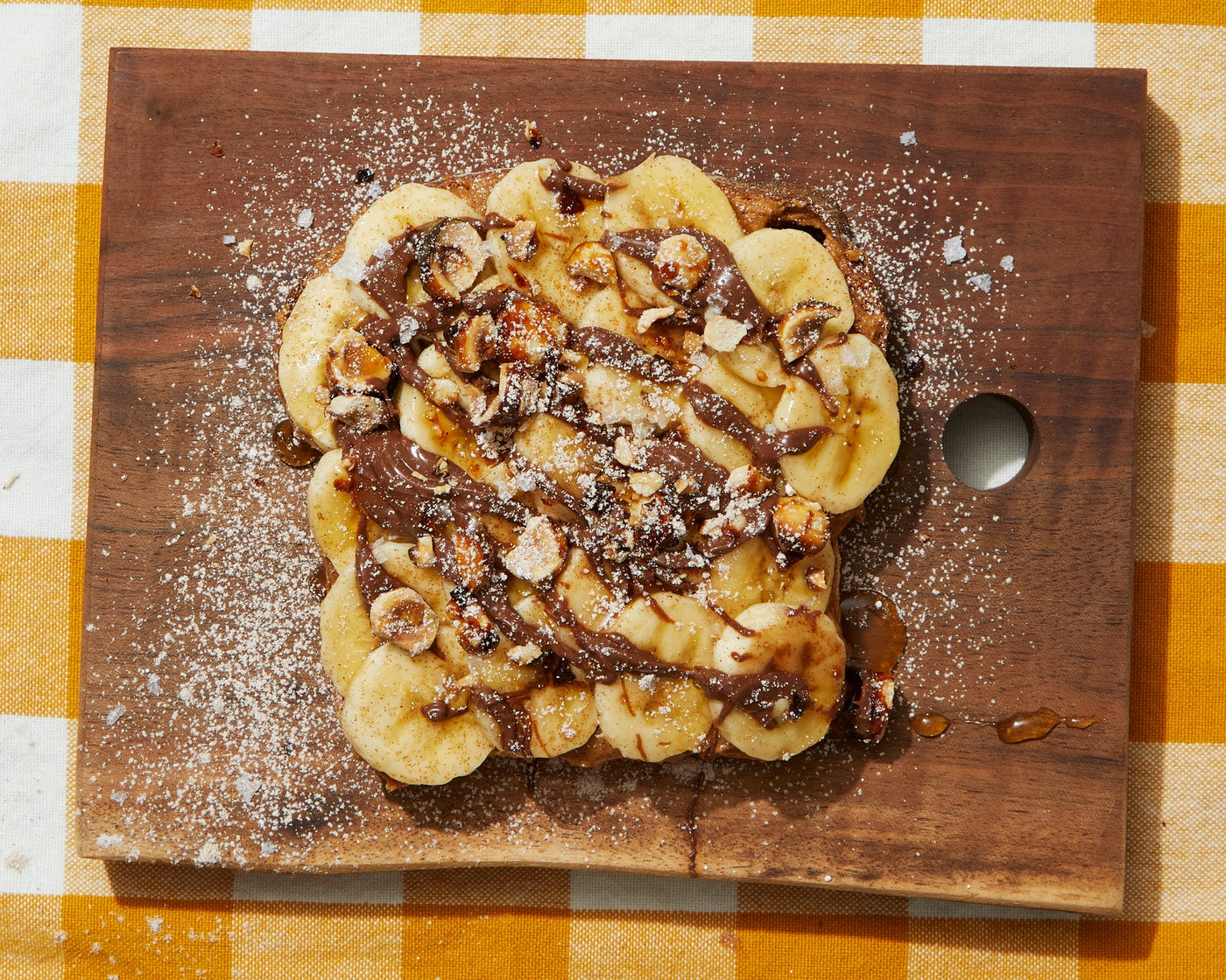 A piece of toast covered in bananas, chocolate, and nuts.