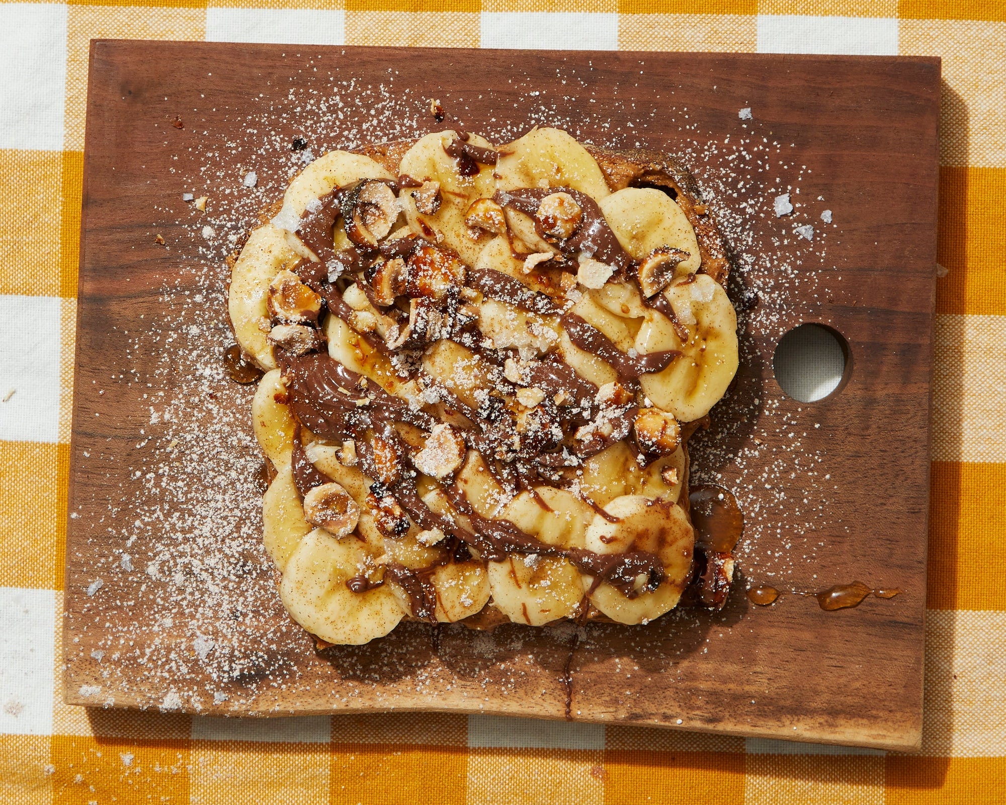 A piece of toast covered in bananas, chocolate, and nuts.