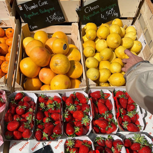 A booth at a farmers market with crates of citrus and strawberries.