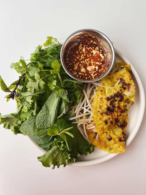 Plated dish, featuring lettuce and cilantro, orange dipping sauce and yellow Banh Xeo.
