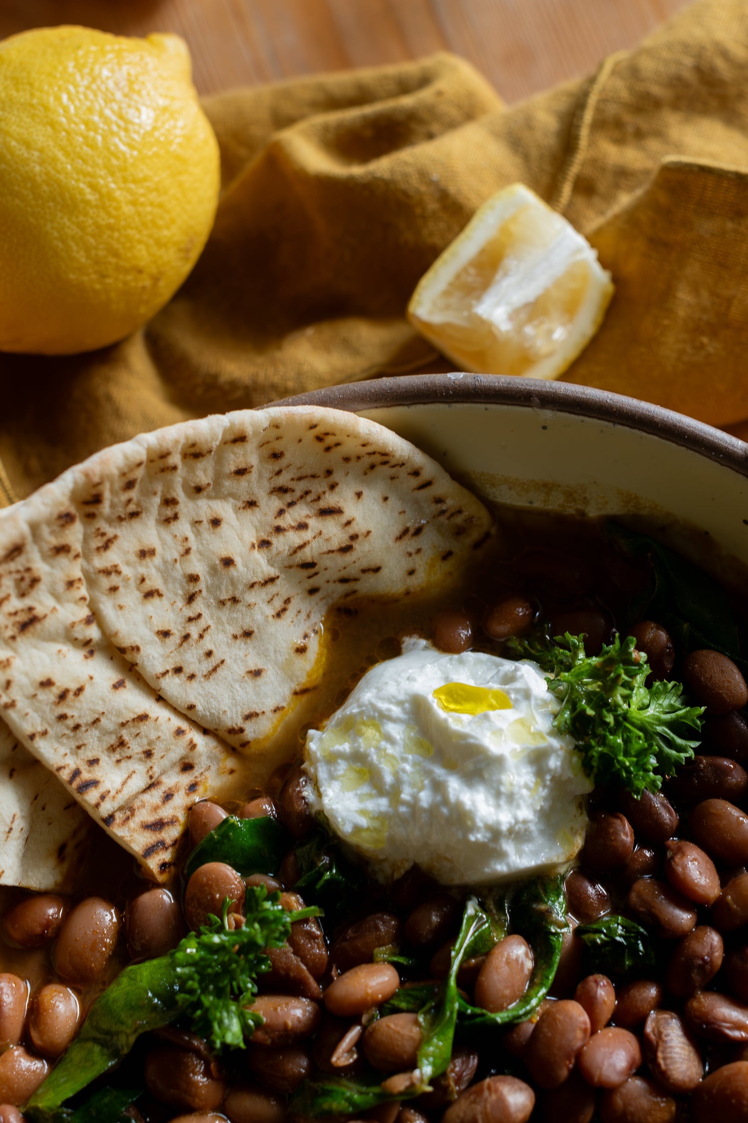 A bowl of beans and greens garnished with yoghurt and flat bread.