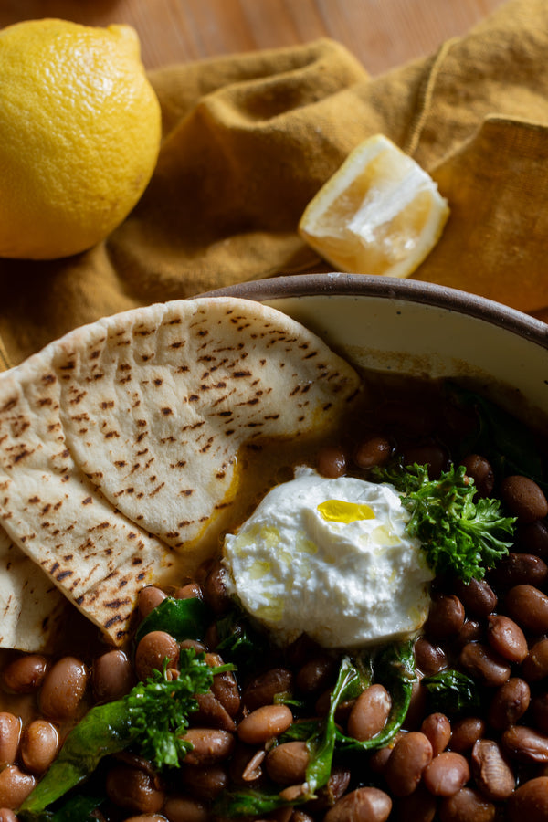 A bowl of beans and greens garnished with yoghurt and flat bread.