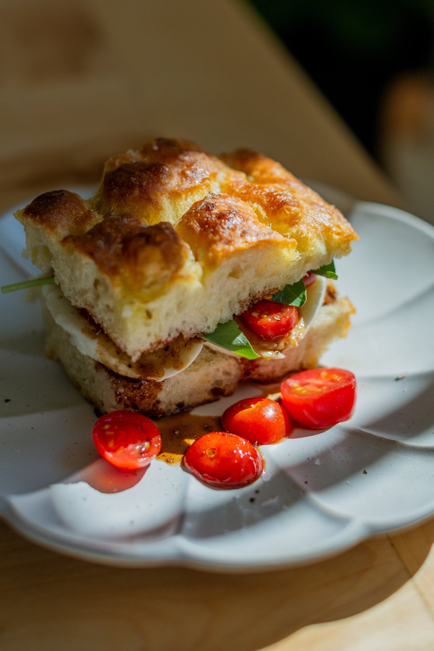 Thick focaccia bread used for a sandwich, plated with sliced cherry tomatoes. 