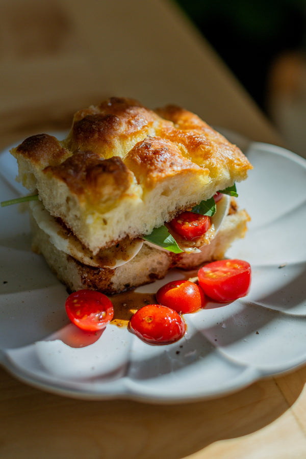 Thick focaccia bread used for a sandwich, plated with sliced cherry tomatoes. 
