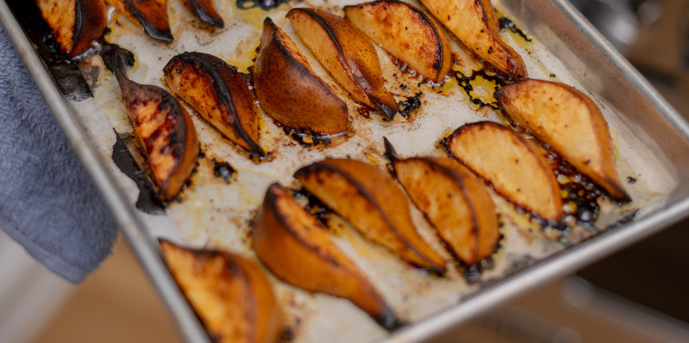 Roasted, golden pears on a baking sheet, with visible seasoning. 