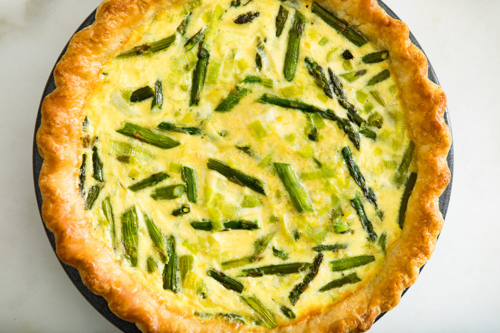 Top view of a yellow Quiche in a circular pan, with visible chopped asparagus.