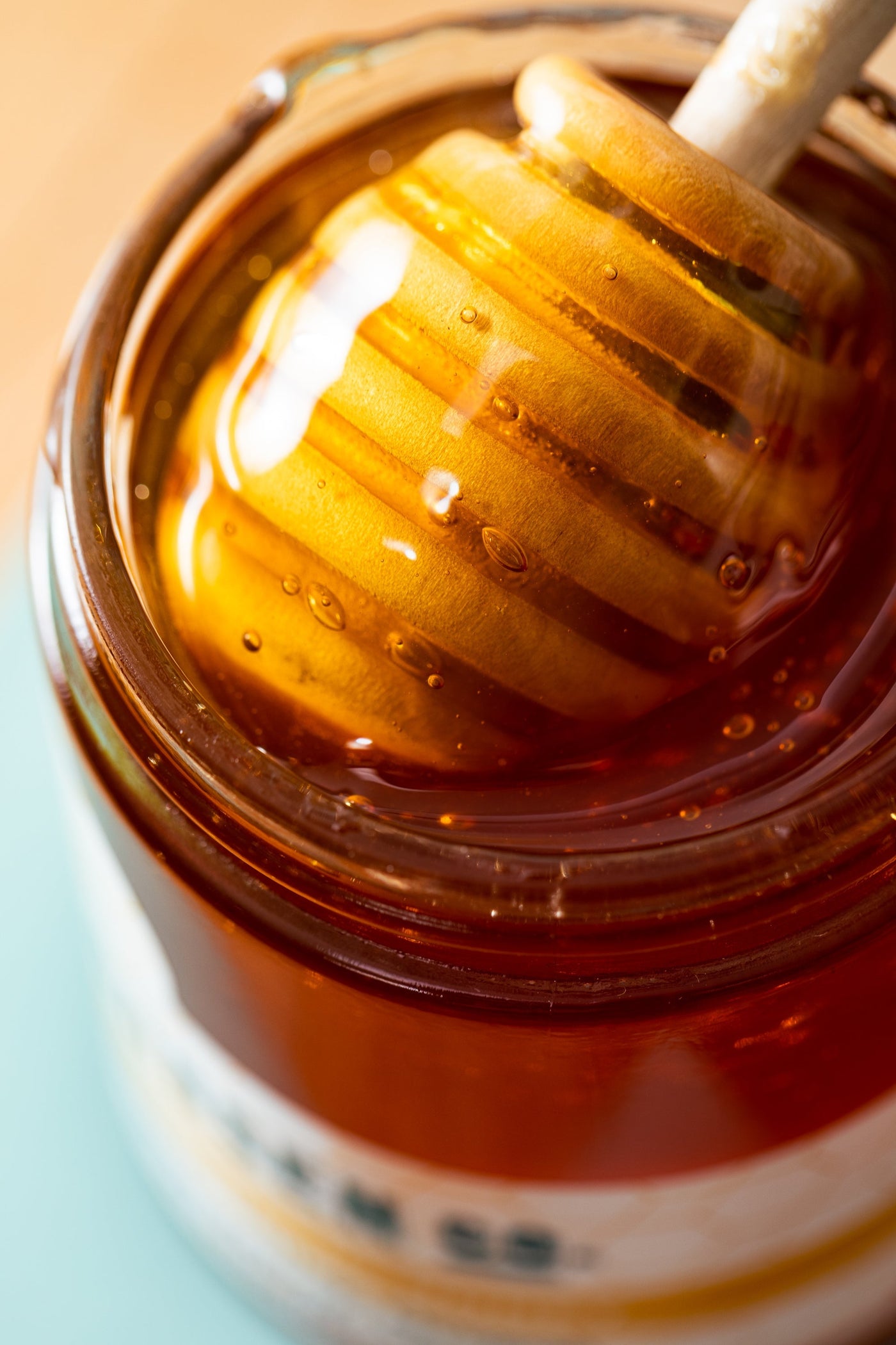 A wooden honey dipper brings honey out of a jar.