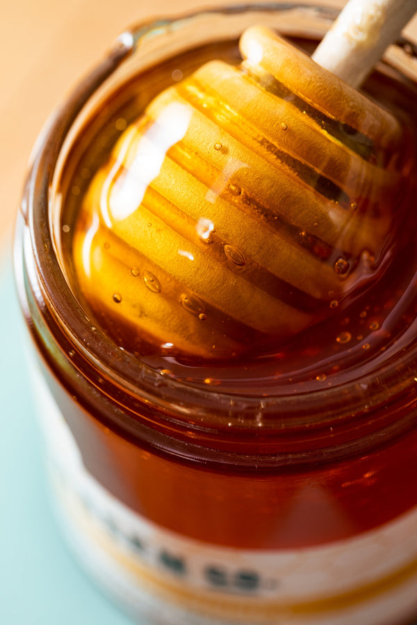 A wooden honey dipper brings honey out of a jar.