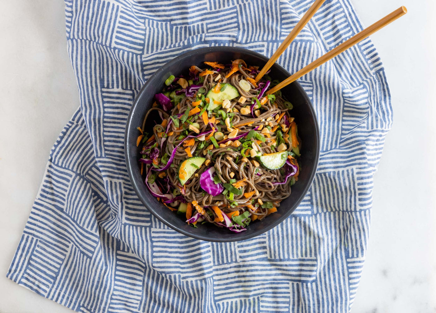 A bowl of soba noodle salad on a kitchen towel.