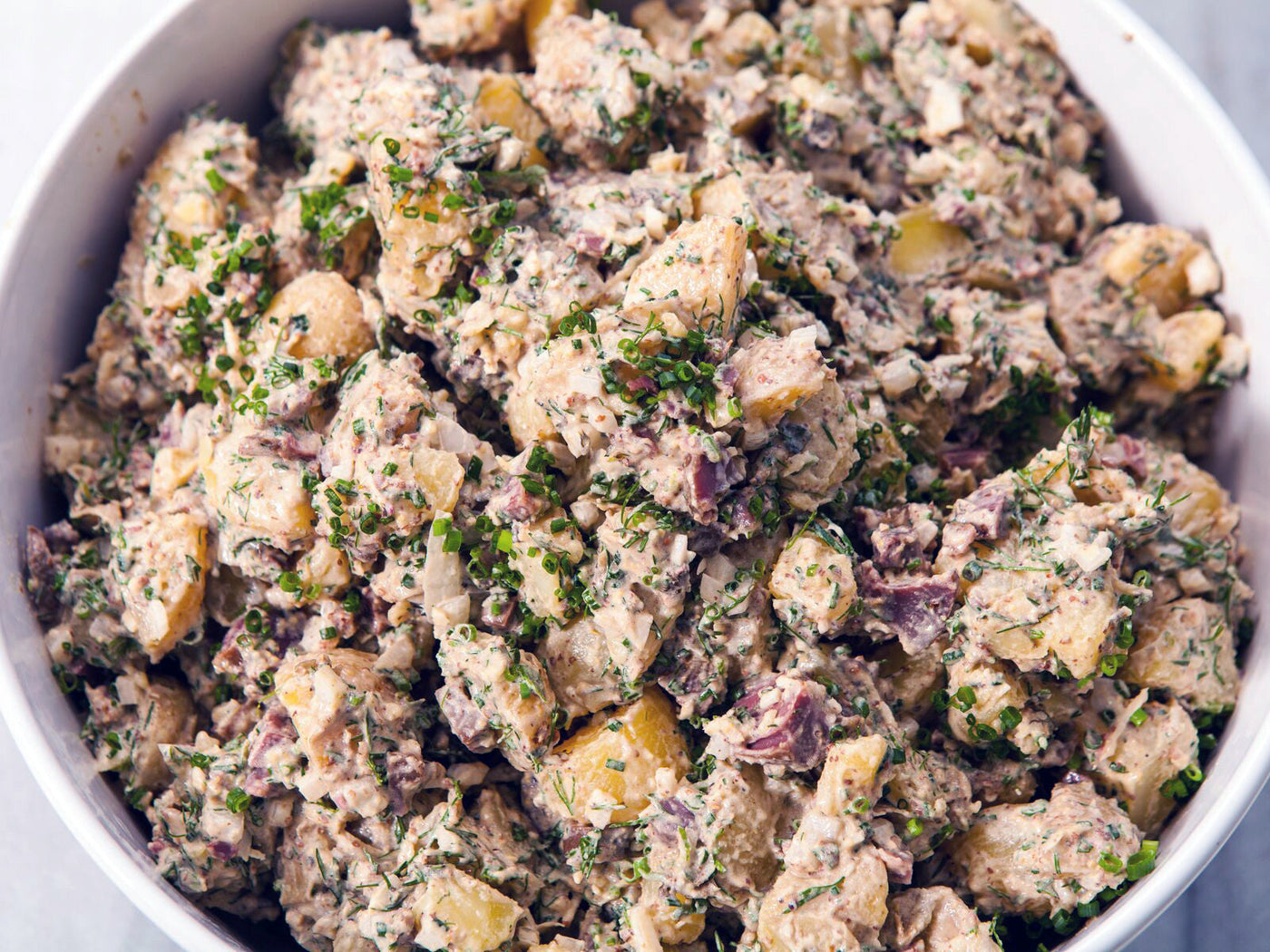 A bowl of small, cut up potatoes mixed together with various seasonings and ingredients.