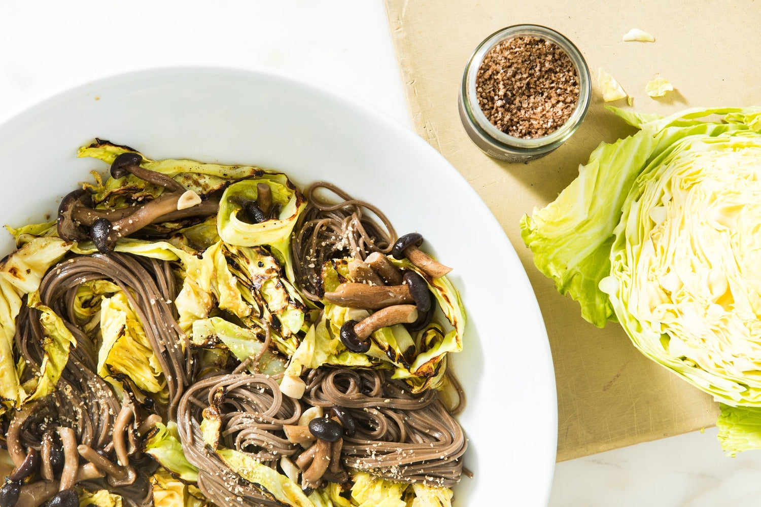 A bowl of soba noodles, a head of cabbage, and a jar of Black Garlic Salt.
