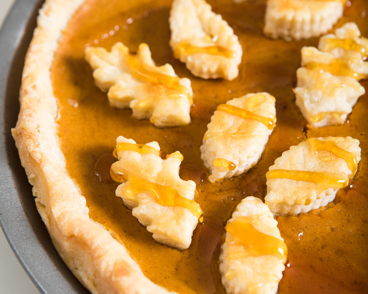 A custard pie with pieces of crust shaped like leaves and a drizzle of honey.