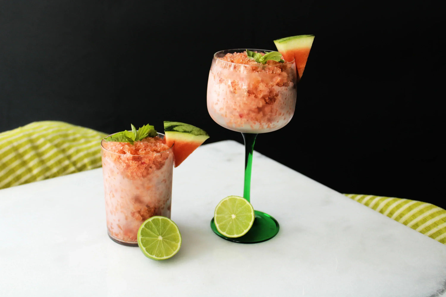 Two glasses of watermelon granita on top of a white table.