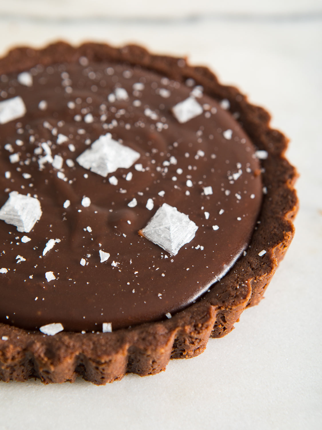 Dark brown, circular peanut butter tart, with very large salt flakes on top.