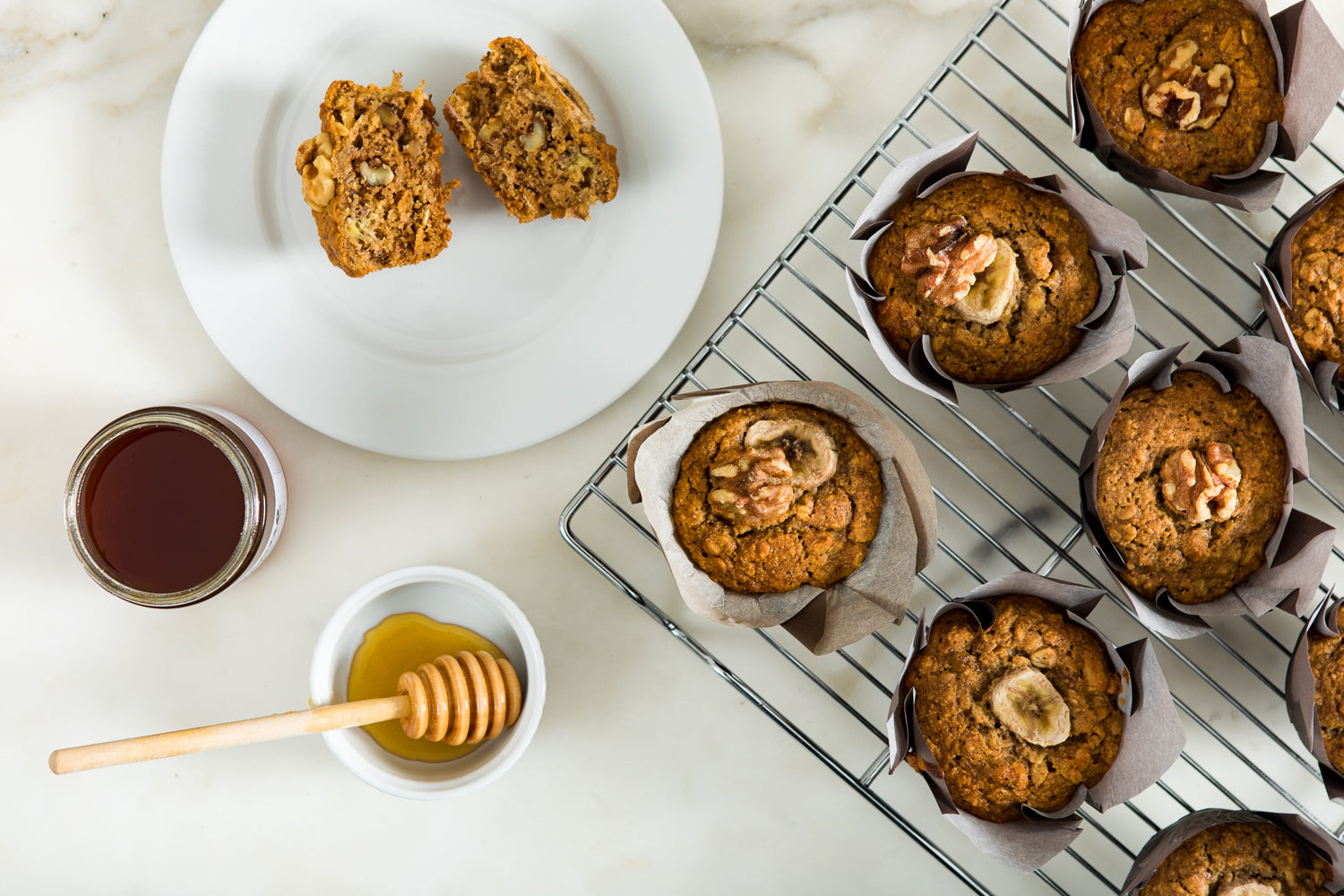 A tray of banana nut muffins, a plate with a muffin cut in half, and an open jar of honey.