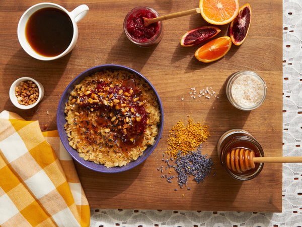 A wooden cutting board with a cup of coffee, a bowl of oatmeal, and toppings.