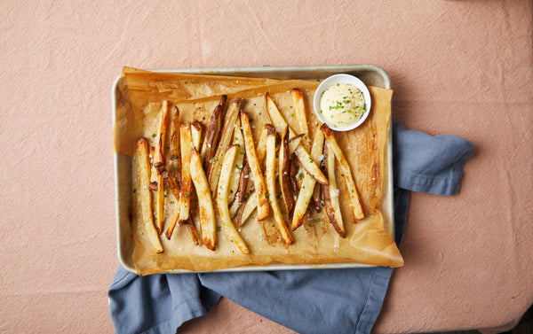 A sheet tray of freshly baked French fries and a bowl of aioli.