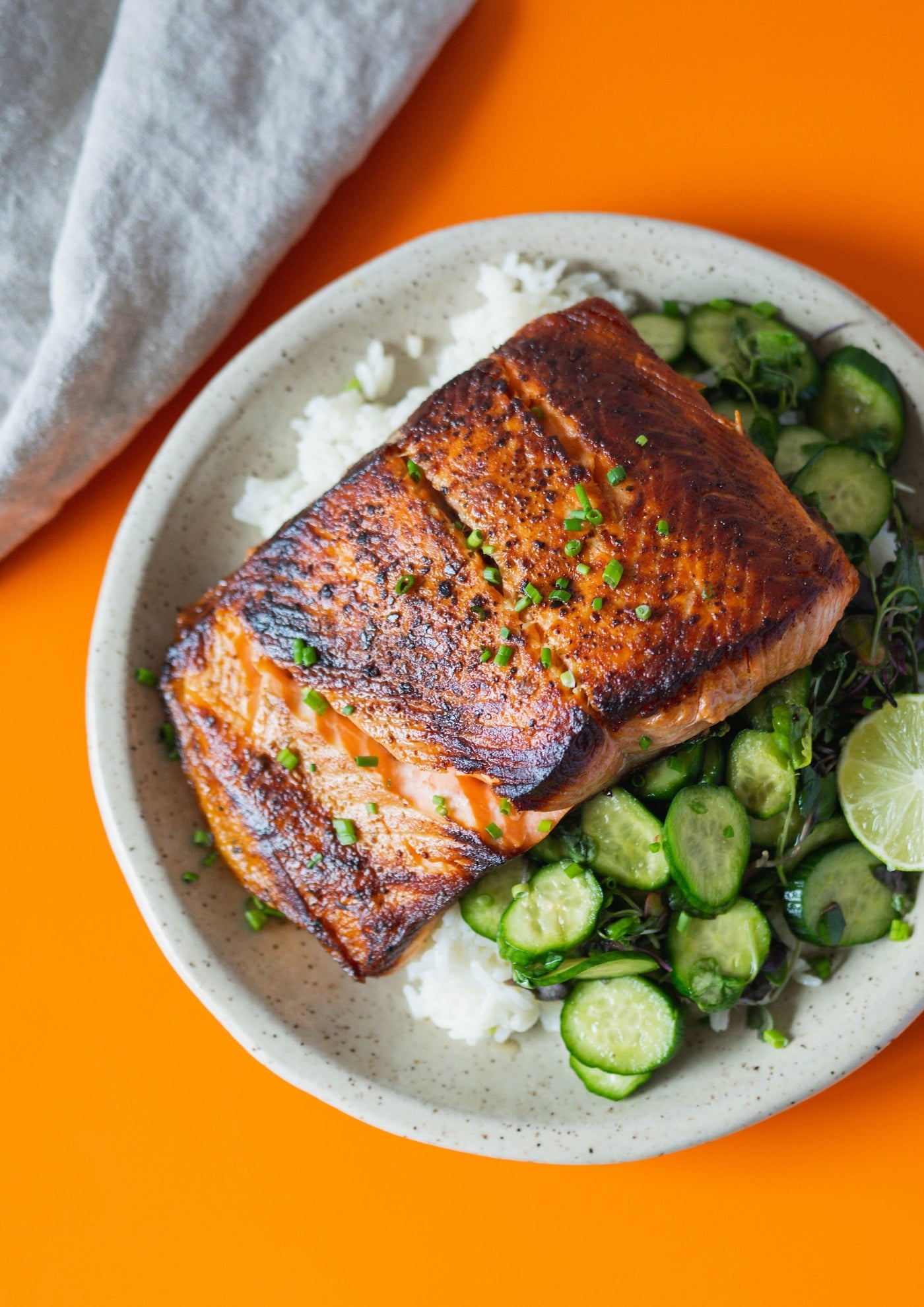 Seared salmon on cucumber salad and rice, plated on a orange tabletop.