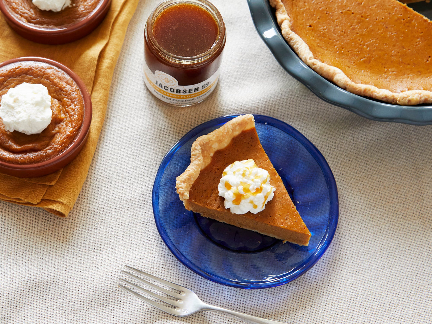 A whole caramelized sweet potato pie, a slice of the same pie, and a jar of honey.