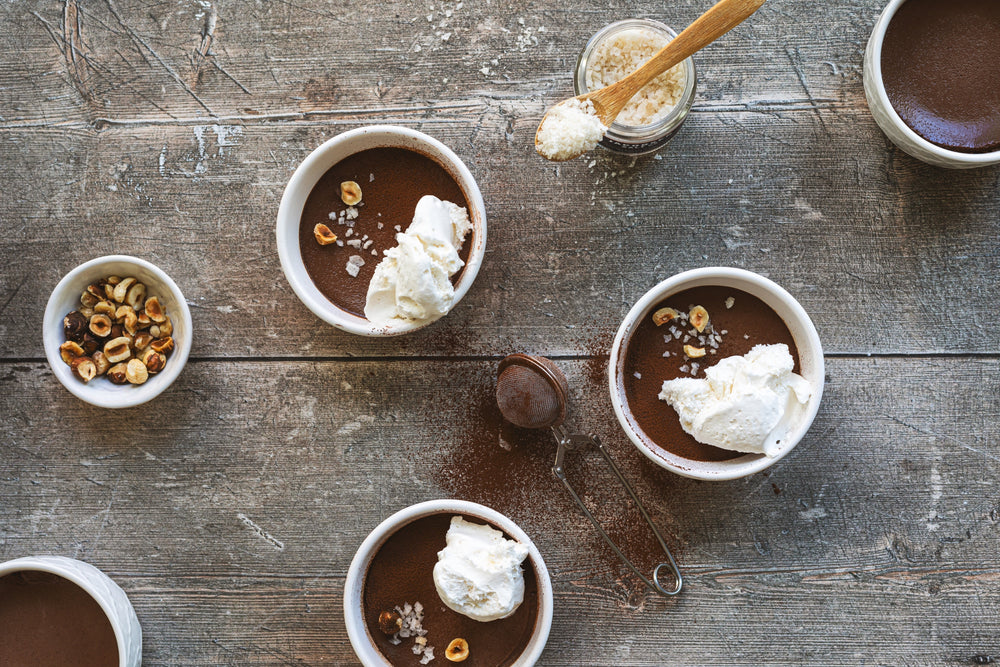 Three bowls of chocolate topped with whipped cream and nut mixture on a rustic wooden tabletop.