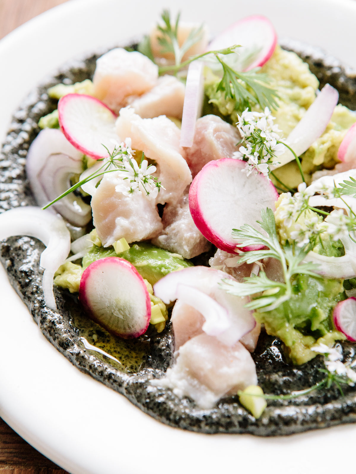 A plate of ceviche, made up of tuna, sliced radishes  and cilantro.